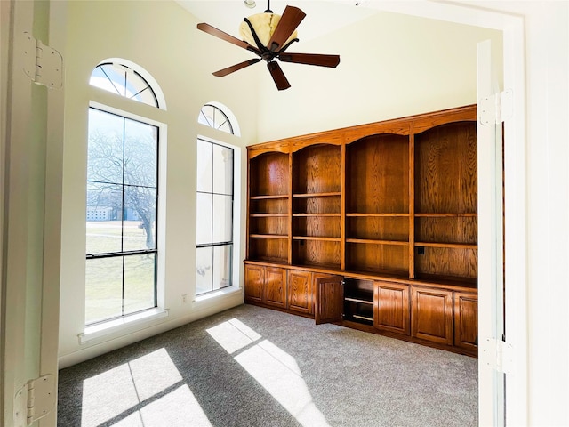 unfurnished living room featuring a towering ceiling, light carpet, and ceiling fan