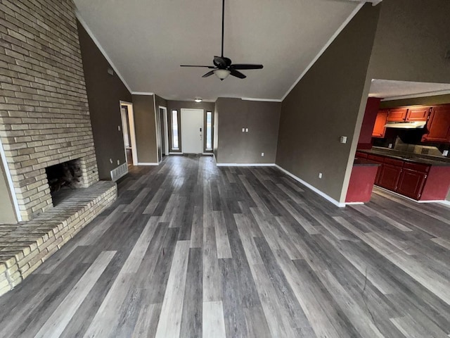 unfurnished living room with dark wood-type flooring, lofted ceiling, ornamental molding, ceiling fan, and a fireplace