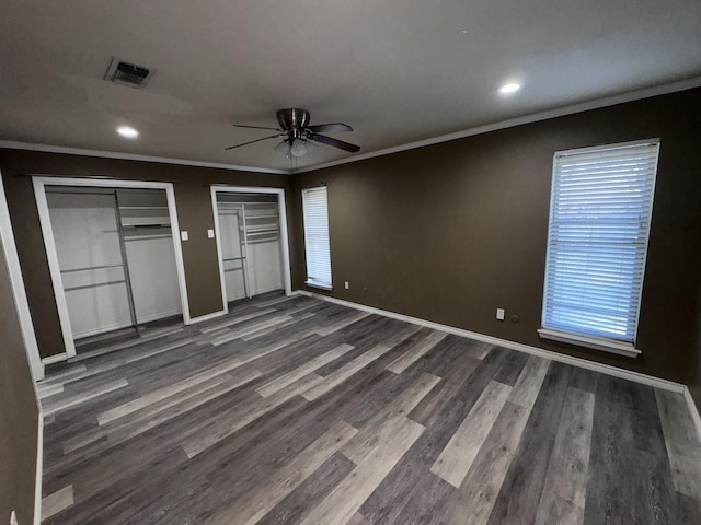 unfurnished bedroom with multiple closets, dark hardwood / wood-style flooring, ornamental molding, and ceiling fan