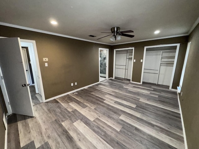 unfurnished bedroom with crown molding, ceiling fan, wood-type flooring, and multiple closets