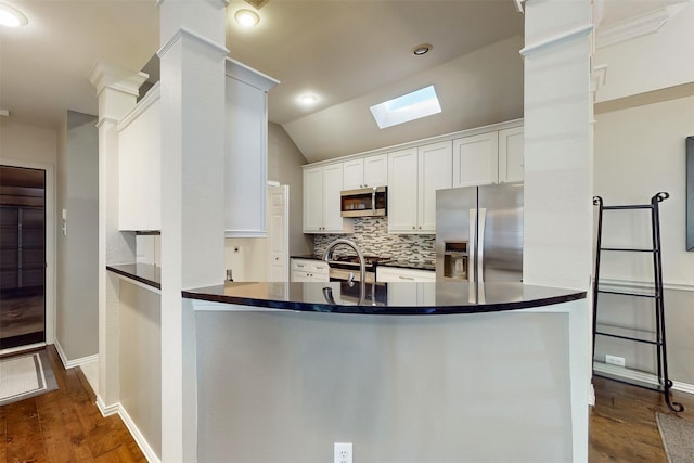 kitchen with appliances with stainless steel finishes, lofted ceiling with skylight, kitchen peninsula, and white cabinets