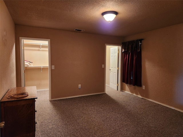 unfurnished bedroom with a spacious closet, carpet floors, a closet, and a textured ceiling