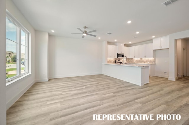 kitchen featuring ceiling fan, white cabinetry, stainless steel appliances, light hardwood / wood-style floors, and decorative backsplash