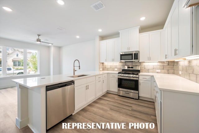 kitchen featuring sink, kitchen peninsula, stainless steel appliances, decorative backsplash, and white cabinets