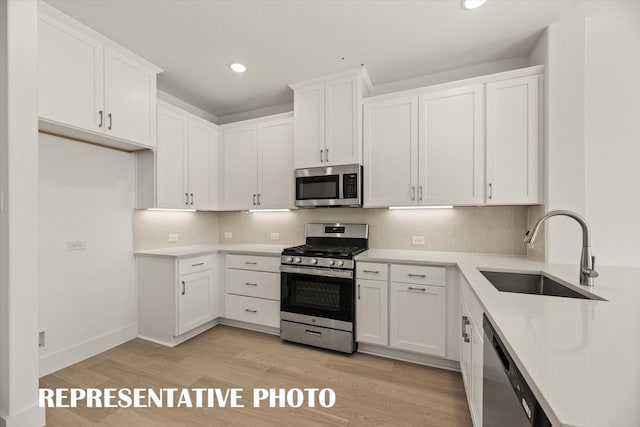 kitchen featuring appliances with stainless steel finishes, sink, backsplash, white cabinets, and light wood-type flooring