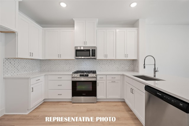 kitchen featuring appliances with stainless steel finishes, tasteful backsplash, sink, white cabinets, and light hardwood / wood-style flooring