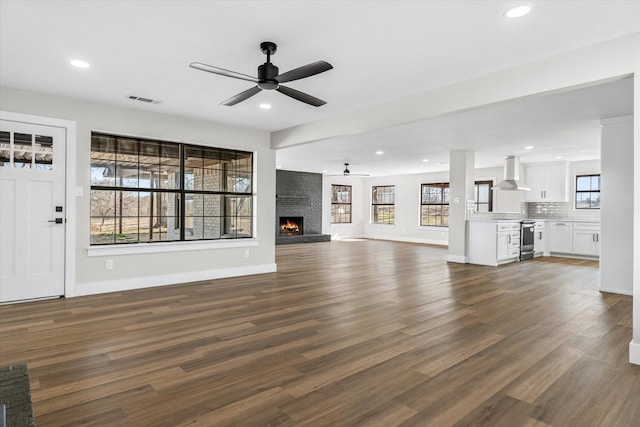 unfurnished living room featuring a brick fireplace, plenty of natural light, and dark hardwood / wood-style floors