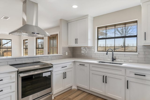 kitchen featuring sink, white cabinetry, island range hood, stainless steel electric range, and light hardwood / wood-style floors