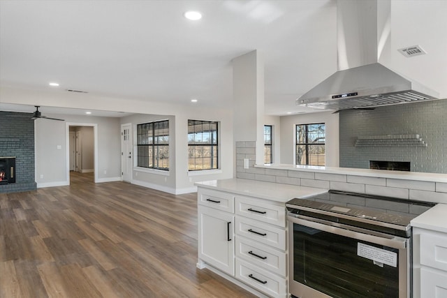 kitchen featuring electric stove, white cabinetry, island range hood, a brick fireplace, and decorative backsplash