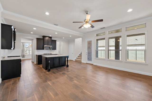 kitchen featuring crown molding, wood-type flooring, a center island with sink, and ceiling fan