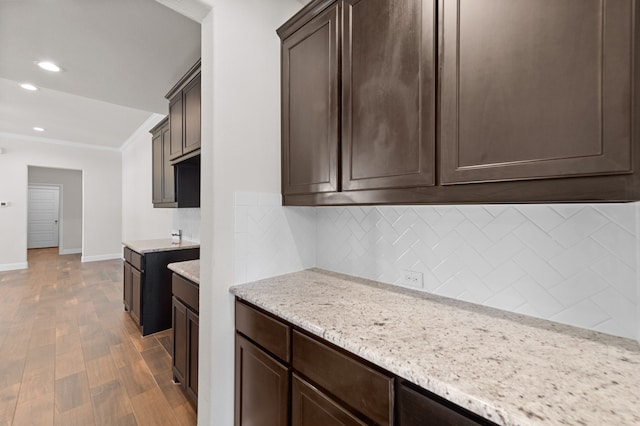 kitchen featuring dark brown cabinetry, backsplash, wood-type flooring, and light stone countertops