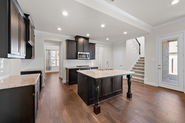 kitchen featuring appliances with stainless steel finishes, a kitchen island with sink, sink, and decorative backsplash