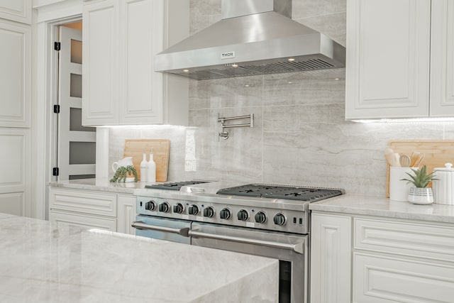 kitchen featuring backsplash, light stone countertops, white cabinets, exhaust hood, and range with two ovens