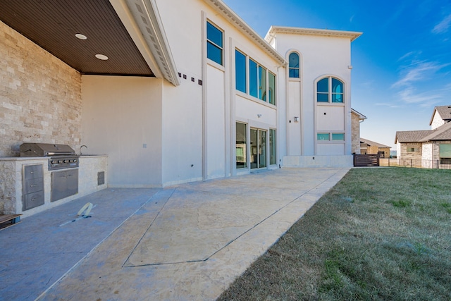 back of property with exterior kitchen, a patio, sink, and a lawn