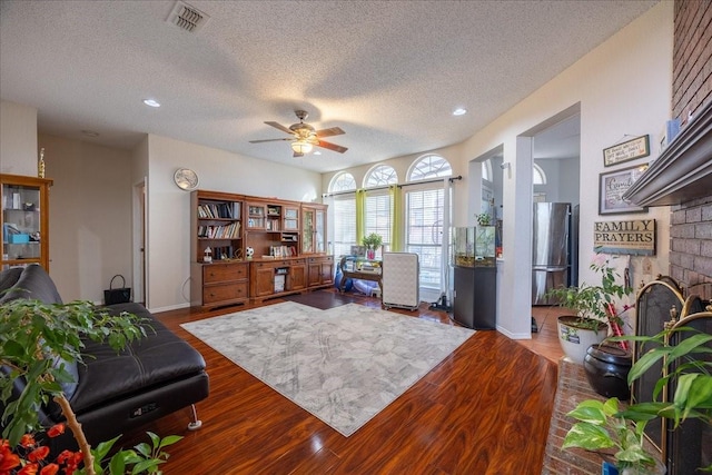 office with a brick fireplace, hardwood / wood-style floors, a textured ceiling, and ceiling fan