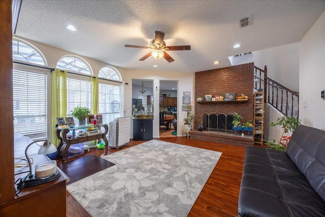 living room with ceiling fan, a fireplace, dark hardwood / wood-style floors, and a textured ceiling