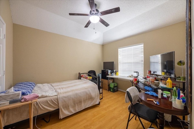 bedroom featuring light hardwood / wood-style flooring, a textured ceiling, vaulted ceiling, and ceiling fan