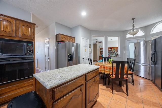 kitchen featuring light tile patterned floors, a center island, black appliances, a textured ceiling, and decorative light fixtures