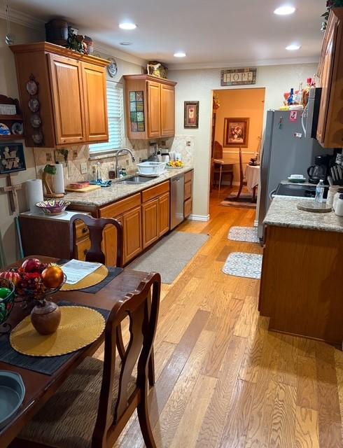 kitchen featuring ornamental molding, sink, stainless steel dishwasher, and light hardwood / wood-style floors