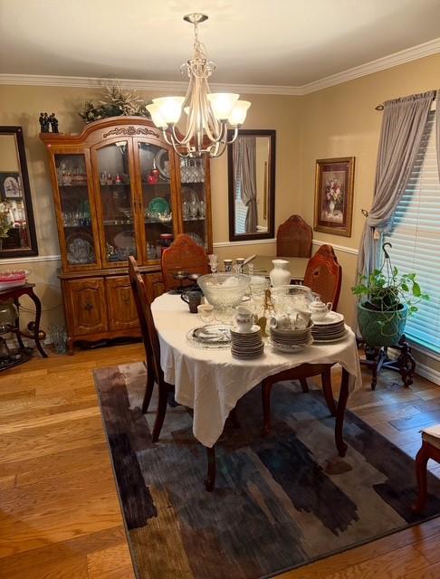 dining space with hardwood / wood-style flooring, crown molding, and a notable chandelier