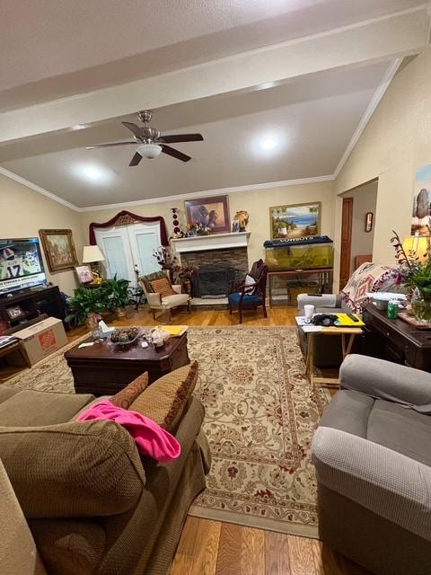 living room with ornamental molding, wood-type flooring, a stone fireplace, and vaulted ceiling