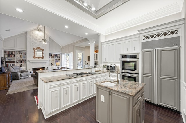 kitchen with an island with sink, black electric stovetop, light stone counters, kitchen peninsula, and stainless steel double oven