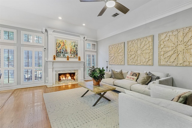 living room featuring wood-type flooring, crown molding, ceiling fan, and a high end fireplace