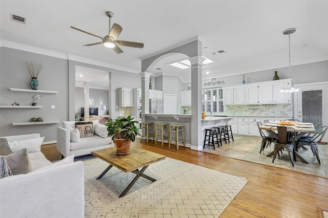 living room with decorative columns, crown molding, and light wood-type flooring