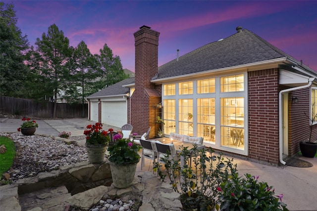 back house at dusk featuring a garage and a patio