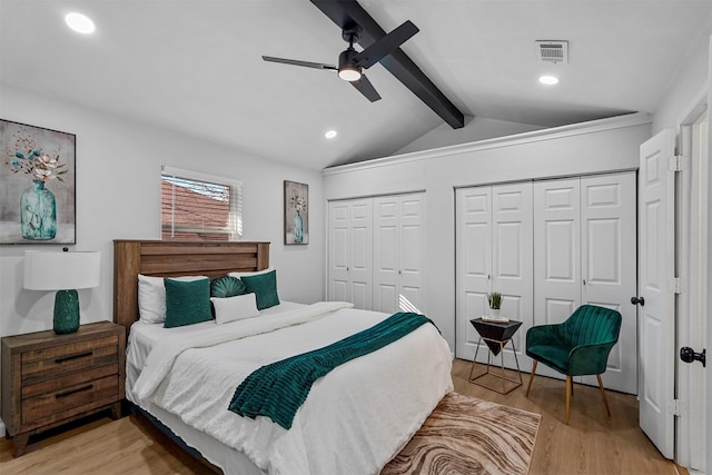 bedroom with ceiling fan, vaulted ceiling with beams, light hardwood / wood-style floors, and multiple closets