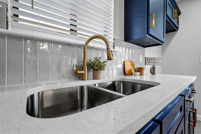 interior details featuring blue cabinetry, sink, light stone countertops, and tasteful backsplash