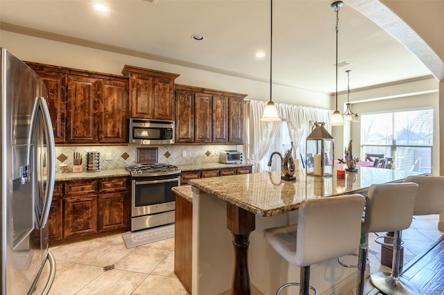 kitchen with a kitchen island with sink, light stone countertops, backsplash, and stainless steel appliances