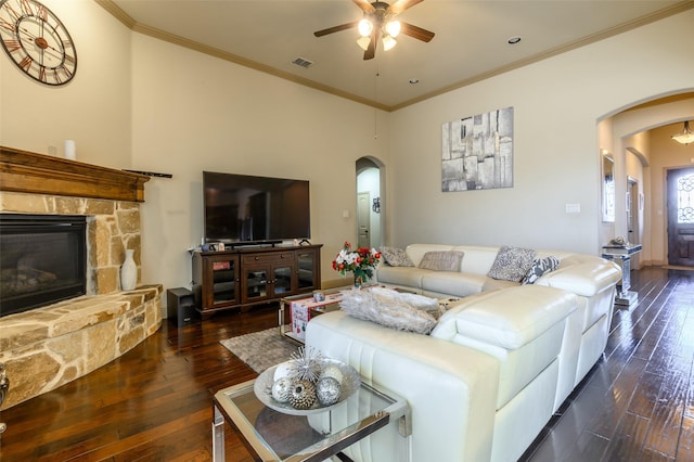 living room with crown molding, a stone fireplace, dark hardwood / wood-style floors, and ceiling fan