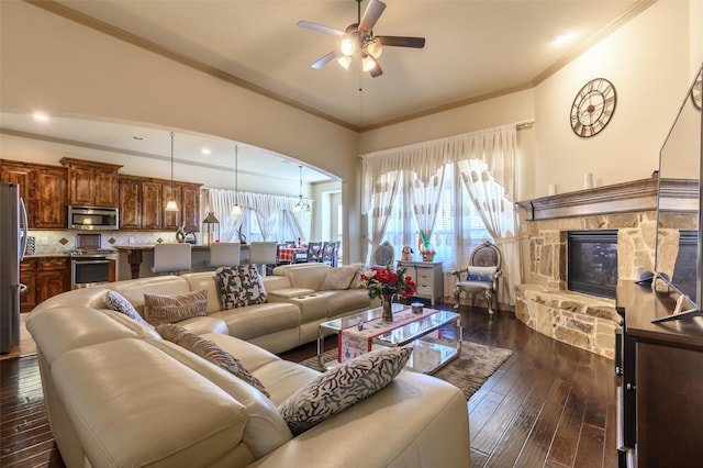 living room featuring crown molding, ceiling fan, a stone fireplace, and dark hardwood / wood-style flooring