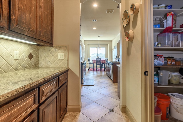 kitchen featuring light tile patterned floors, crown molding, hanging light fixtures, backsplash, and light stone counters