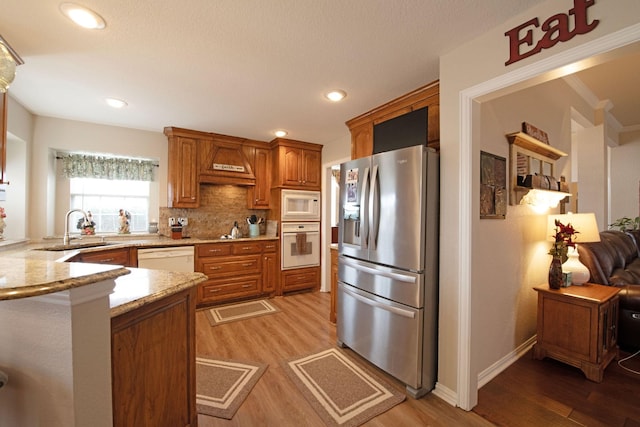 kitchen featuring premium range hood, sink, light wood-type flooring, white appliances, and backsplash