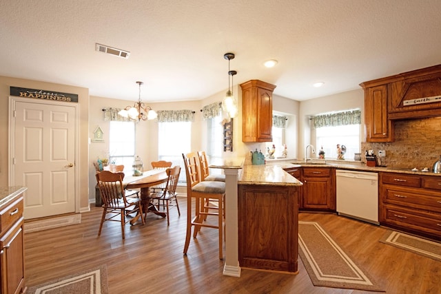 kitchen with a breakfast bar area, tasteful backsplash, hardwood / wood-style flooring, white dishwasher, and pendant lighting