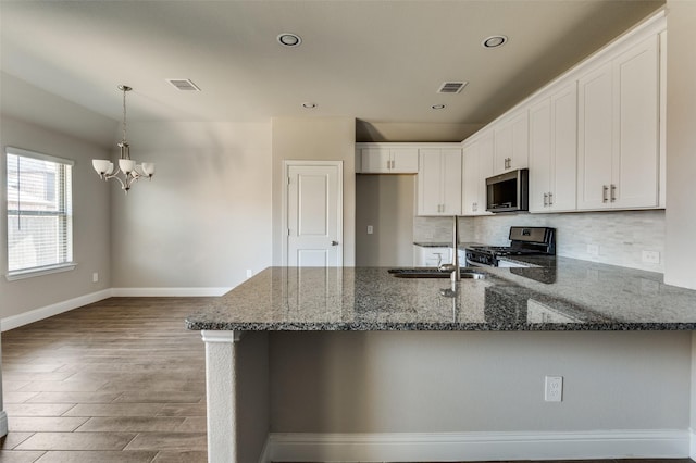 kitchen featuring pendant lighting, stove, backsplash, white cabinetry, and dark stone countertops