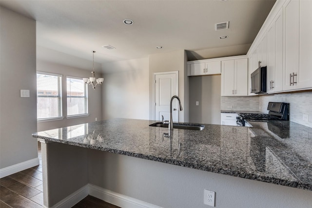 kitchen featuring decorative light fixtures, sink, white cabinets, dark stone counters, and gas range oven