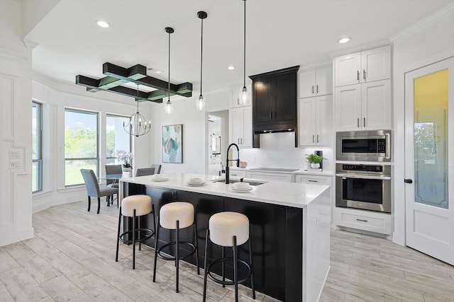 kitchen with white cabinetry, decorative light fixtures, appliances with stainless steel finishes, an island with sink, and beam ceiling