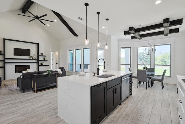 kitchen with sink, decorative light fixtures, light wood-type flooring, and a center island with sink