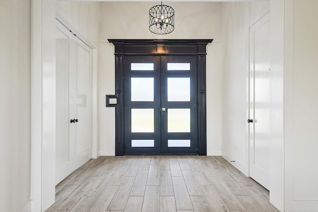 entrance foyer with an inviting chandelier, light hardwood / wood-style floors, and french doors