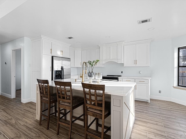 kitchen with a kitchen bar, white cabinetry, stainless steel fridge with ice dispenser, custom range hood, and a kitchen island with sink