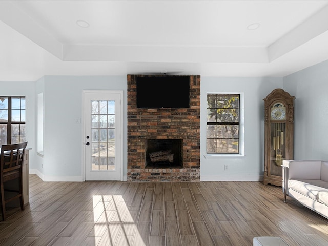 unfurnished living room with a brick fireplace, a tray ceiling, and a healthy amount of sunlight