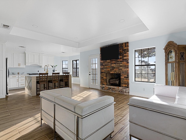 living room featuring a brick fireplace and a tray ceiling