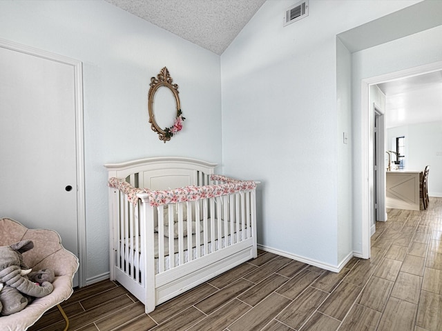 bedroom with vaulted ceiling, a textured ceiling, and a crib