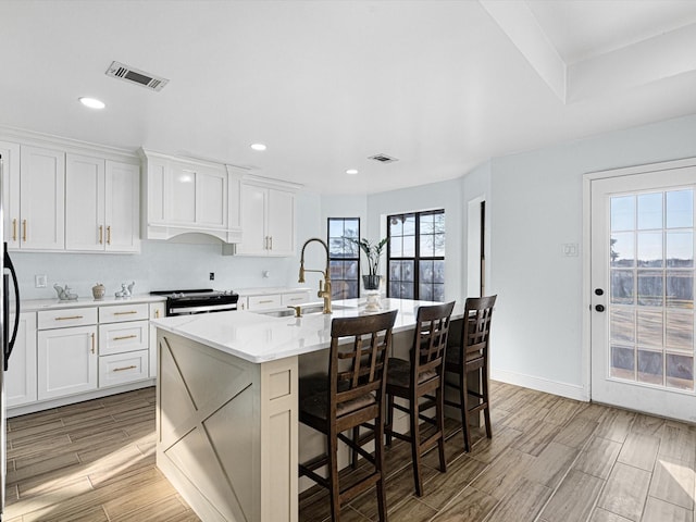 kitchen with an island with sink, sink, white cabinets, a kitchen bar, and electric range