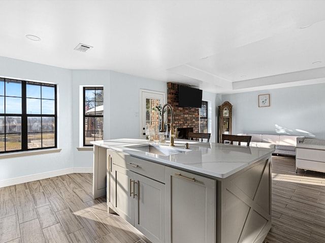 kitchen with sink, a center island with sink, a fireplace, and light stone counters