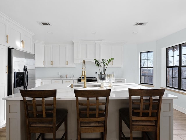 kitchen with a center island with sink, stainless steel fridge, and a kitchen bar