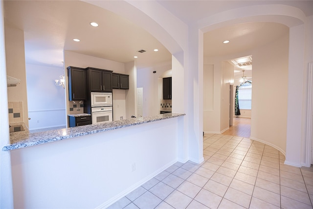 kitchen with light stone counters, light tile patterned floors, white appliances, and kitchen peninsula